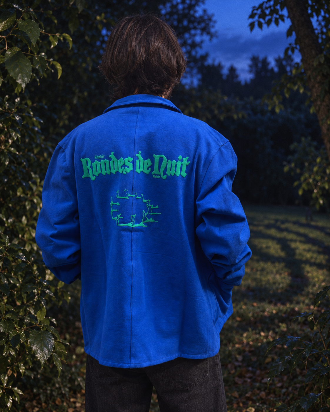 Veste Rondes de nuit portée de dos dans un jardin au crépuscule, mise en scène inspirée du livre.